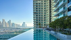 A modern hotel with a long, reflective infinity pool and a view of a city skyline. - Glamorous 3BR With Marina View (Dubai)