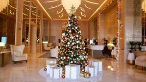A lobby with a large Christmas tree surrounded by gift boxes, a reception desk, and modern furnishings. - Bird S-eye View Studio Palmtower (Dubai)