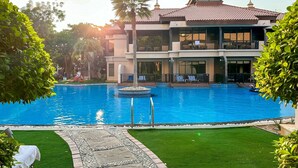 A large swimming pool with a stone pathway leading to a building with a tiled roof and balconies. - Renovated 1BR Haven in 5 Star Resort (Dubai)