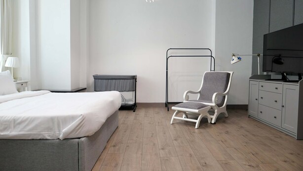 Een hotelkamer met een bed, een grijze fauteuil, een televisie, een bureau met een lamp en een kledingkast.