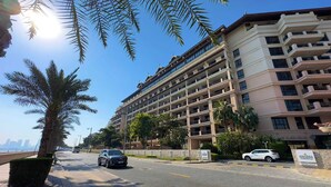 A multi-story hotel with balconies, a paved street, and palm trees. - Upgraded 2BR - Beachfront - 5 Star Resort (Dubai)