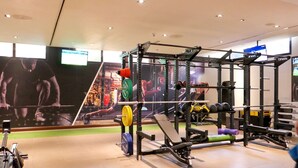 Et fitnessrum med styrketræningsudstyr, løbebånd og en væg med træningsplakater.