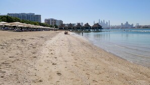A beach with sun loungers and umbrellas, a water body, and a city skyline in the background. - Picture-perfect 2BR Apartment With Burj View (Dubai)