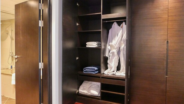 A walk-in closet with multiple shelves and hanging space, a shower area, and a wooden floor. - Picture-perfect 2BR Apartment With Burj View (Dubai)