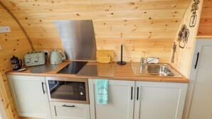 Eine kleine Küche mit Holzwänden, einer Edelstahl-Dunstabzugshaube, einem Spülbecken, einem Toaster und einer Kaffeemaschine.