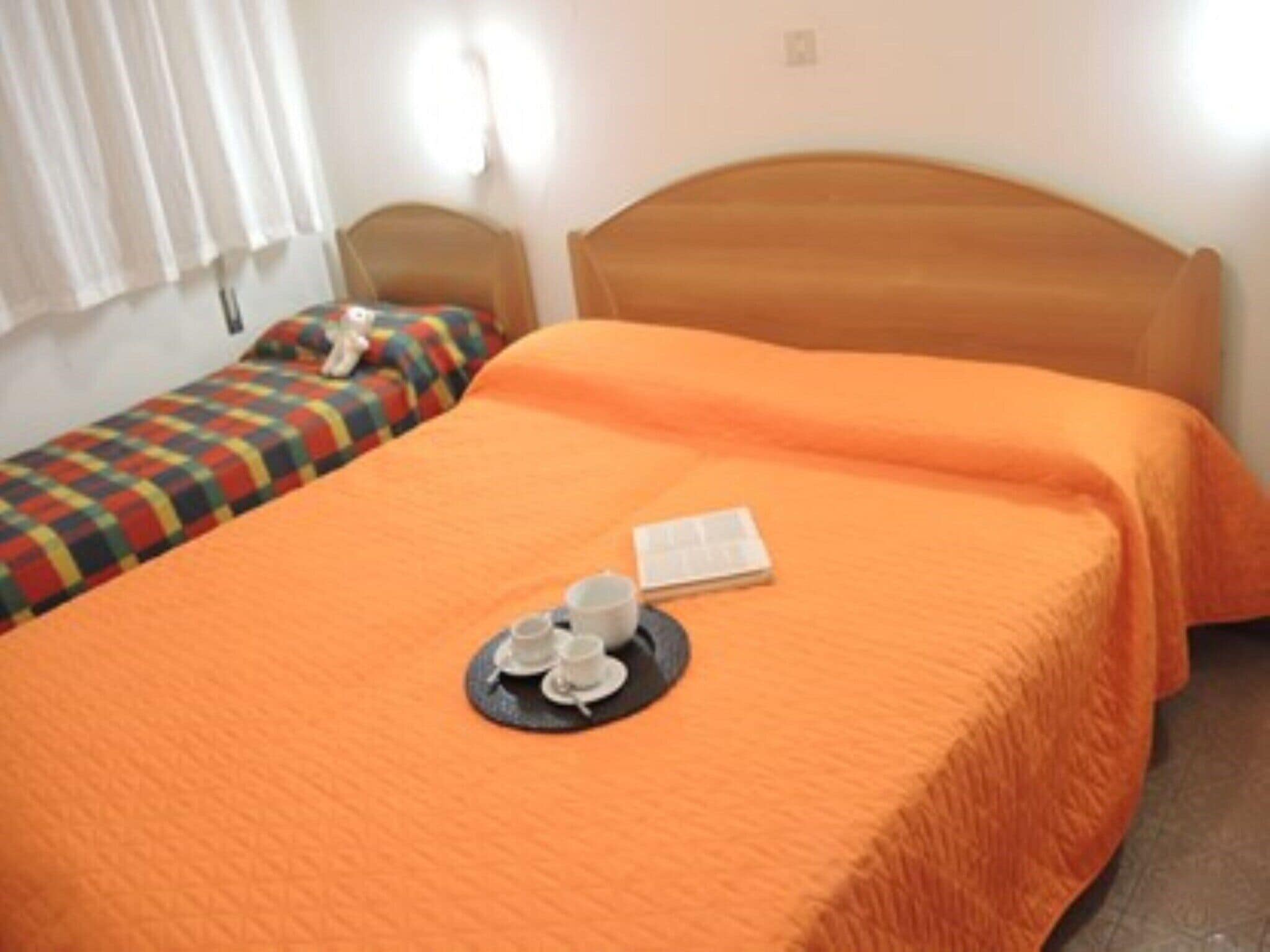 A single bed with an orange bedspread and a tray with cups and a book on it.