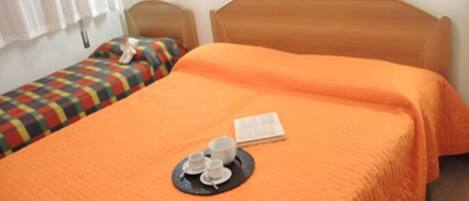 Un lit simple avec une couverture orange et un plateau sur lequel se trouvent des tasses et un livre.