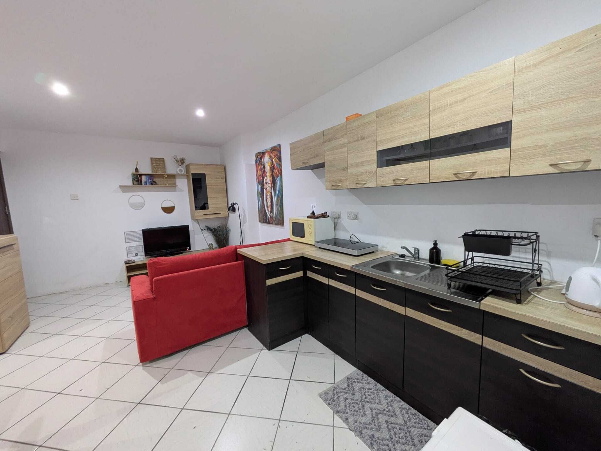 Una cocina moderna con armarios negros y de madera, un sofá rojo y suelo de baldosas.