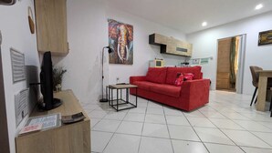 A living room with a red sofa, a small table, a TV, and a painting on the wall. - Valletta Cosy Apartment (Valletta)