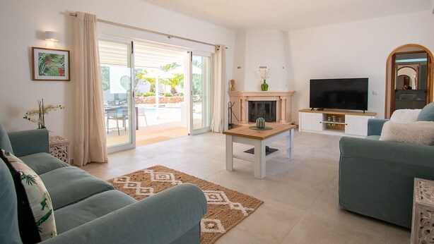 A living room with a sofa, a TV, a fireplace, and a sliding glass door leading to an outdoor area. - Pomba Beautifully Renovated With Heated Pool (Lagoa)