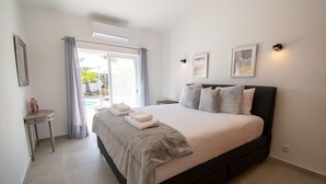 A bedroom with a large bed, a small bedside table, a window with curtains, and a view of the outdoors. - Pomba Beautifully Renovated With Heated Pool (Lagoa)