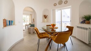 A dining area with a glass table, four chairs, and a vase with dried plants. - Pomba Beautifully Renovated With Heated Pool (Lagoa)