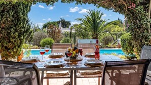Un espace extérieur aménagé pour les repas, avec vue sur une piscine, entouré d’une végétation luxuriante et agrémenté d’une pergola.