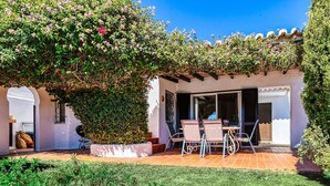 Un espace patio aménagé avec une table et des chaises, entouré de verdure et agrémenté d’une pergola couverte de plantes à fleurs.