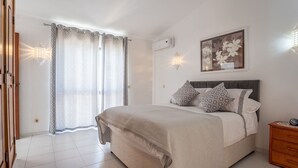 A bedroom with a bed, curtains, a wall-mounted light, a painting, and a bedside table. - Carosim Quiet Location Close to Beach Private (Lagoa)