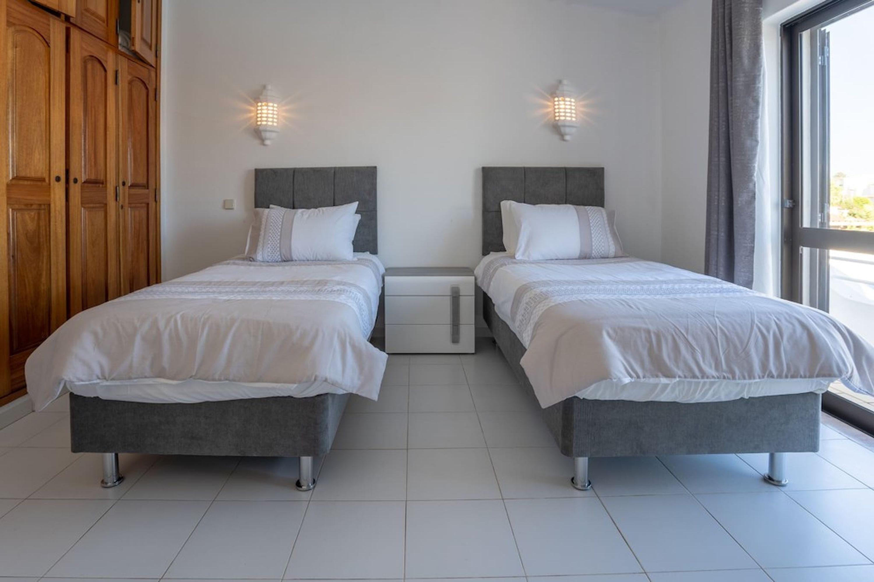 Quarto com duas camas, guarda-roupa de madeira e janela com cortinas.