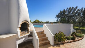 A modern outdoor kitchen with a brick oven, a pool, and a landscaped garden.