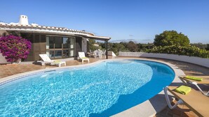 A swimming pool with lounge chairs, a patio area, and a house with a tiled roof.