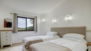 A bedroom with two beds, a nightstand, a dresser, and a window with curtains.