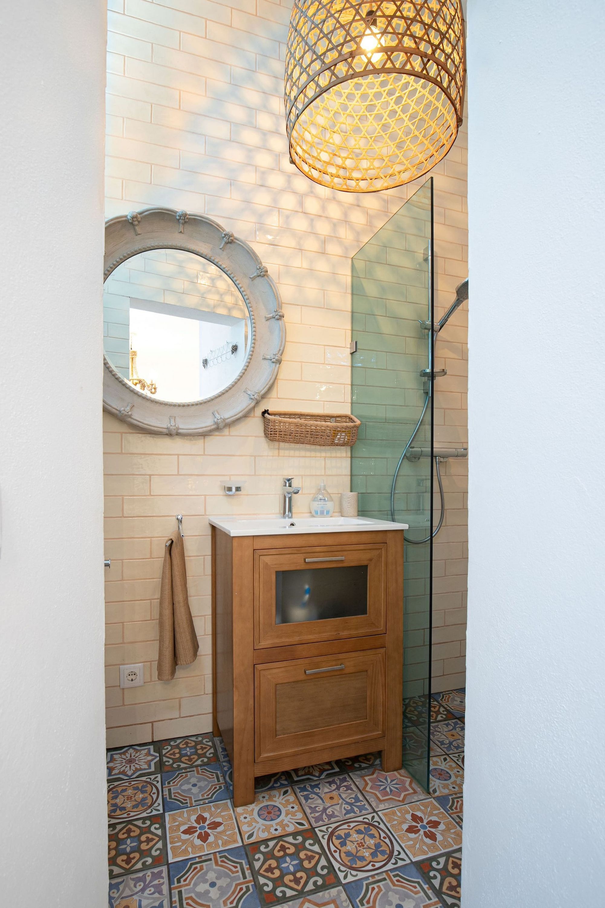 A bathroom with a wooden vanity, a round mirror, a hanging light fixture, and patterned floor tiles.