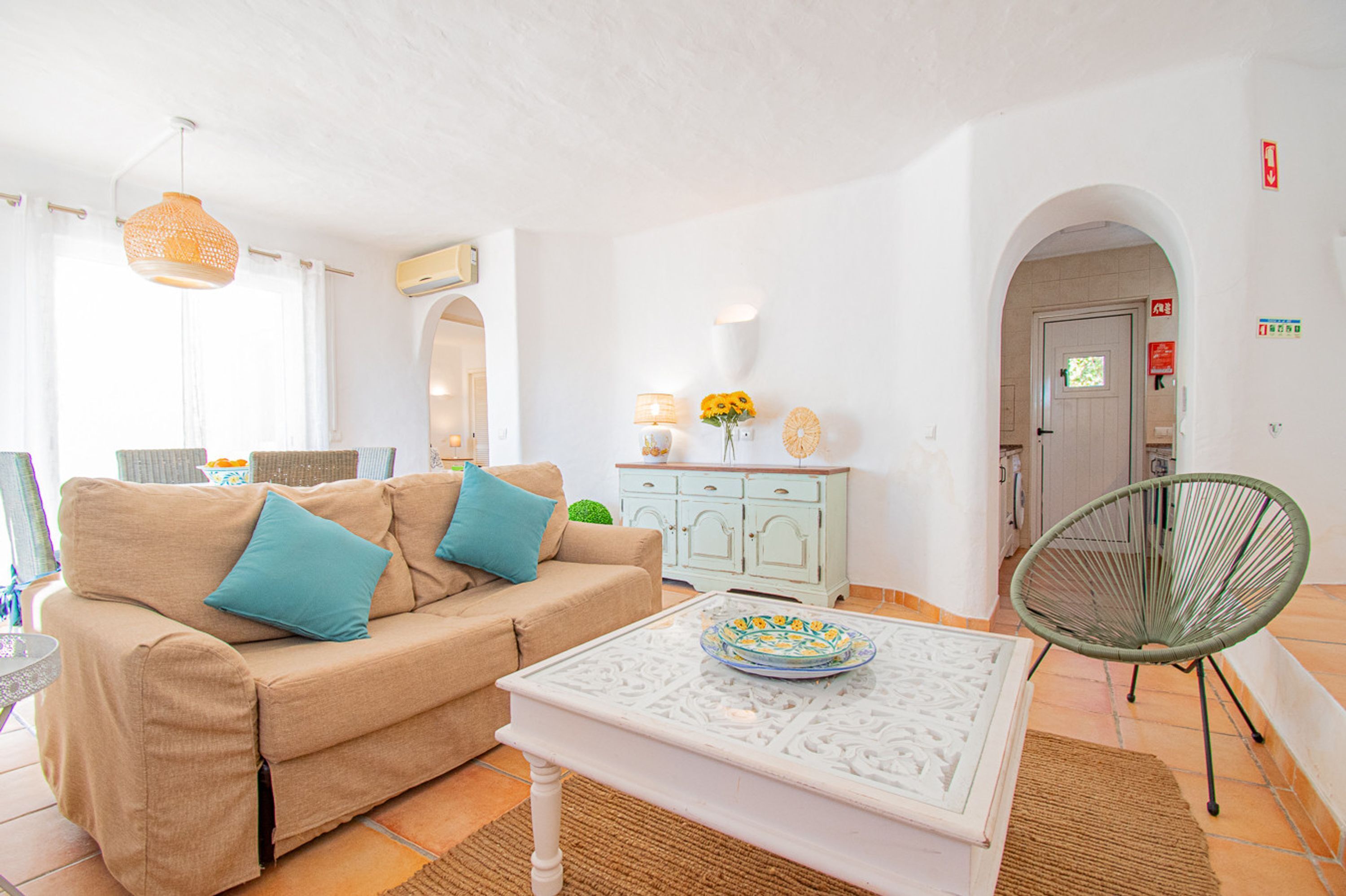 A living room with a sofa, a coffee table, a wicker chair, a cabinet, and a door with an archway.