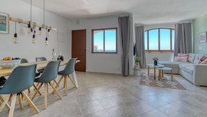 Un salon moderne avec un canapé, un coin repas comprenant une table et des chaises, et une grande fenêtre avec des rideaux.