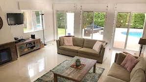 A spacious living room with a sofa, a coffee table, and a TV. There is a sliding glass door leading to an outdoor area with a pool. - 16 Centeanes Fabulous Location Just Short Walk t (Lagoa)