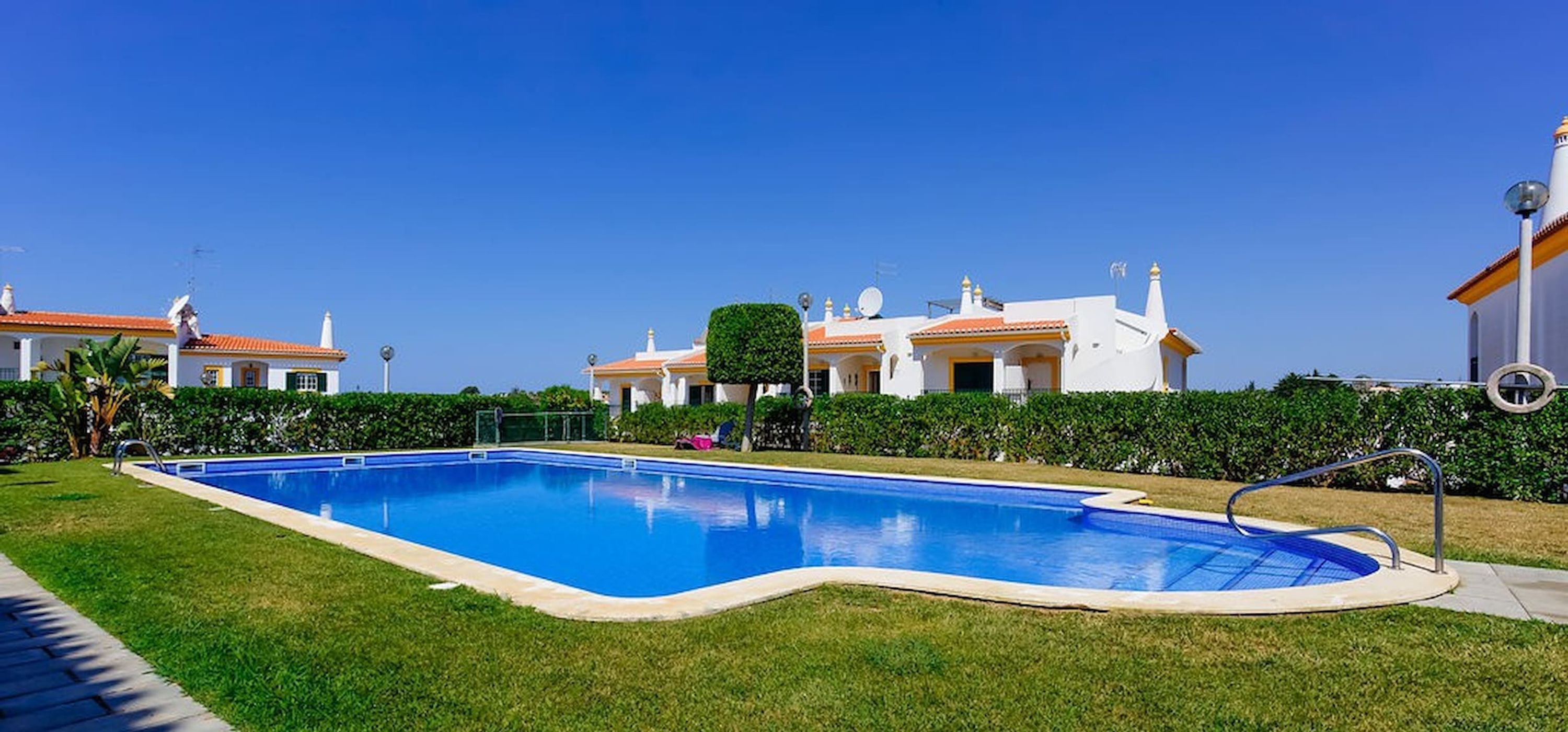 A swimming pool surrounded by well-maintained grass and a row of white buildings with orange roofs.