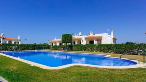 A swimming pool surrounded by well-maintained grass and a row of white buildings with orange roofs.
