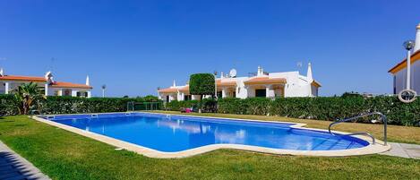 A swimming pool surrounded by well-maintained grass and a row of white buildings with orange roofs.