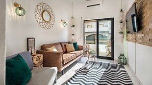 A modern living room with a brown sofa, a striped rug, and a large window with a view of a balcony. - 212 Aurora sol Casinha DO SOL (Lagoa)