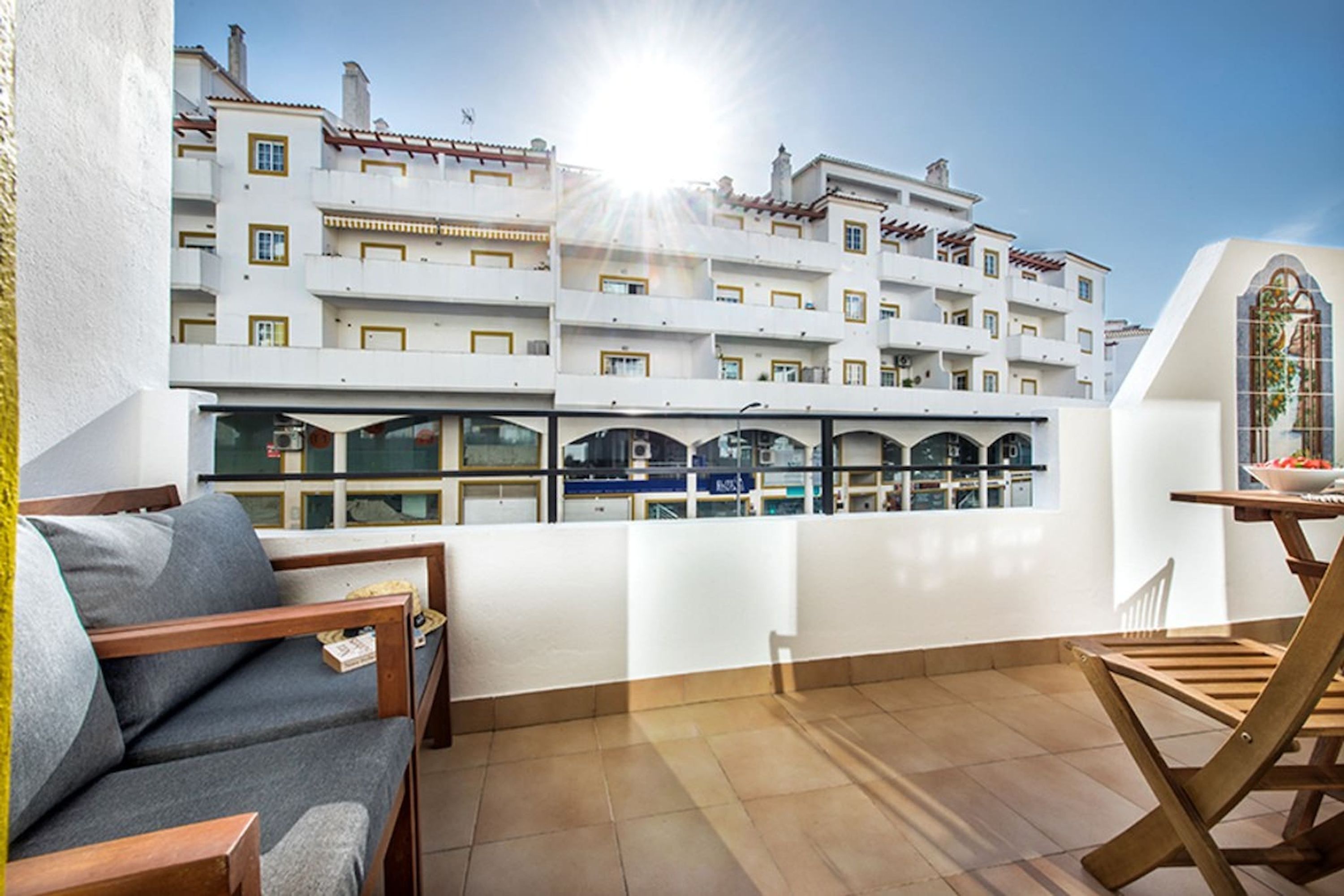 A balcony with a sofa, a wooden table, and a view of a white building with multiple balconies.