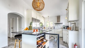 A modern kitchen with white cabinetry, a wine rack, and a large island with stools. - Toupeira Wonderful Well Furnished Villa (Lagoa)