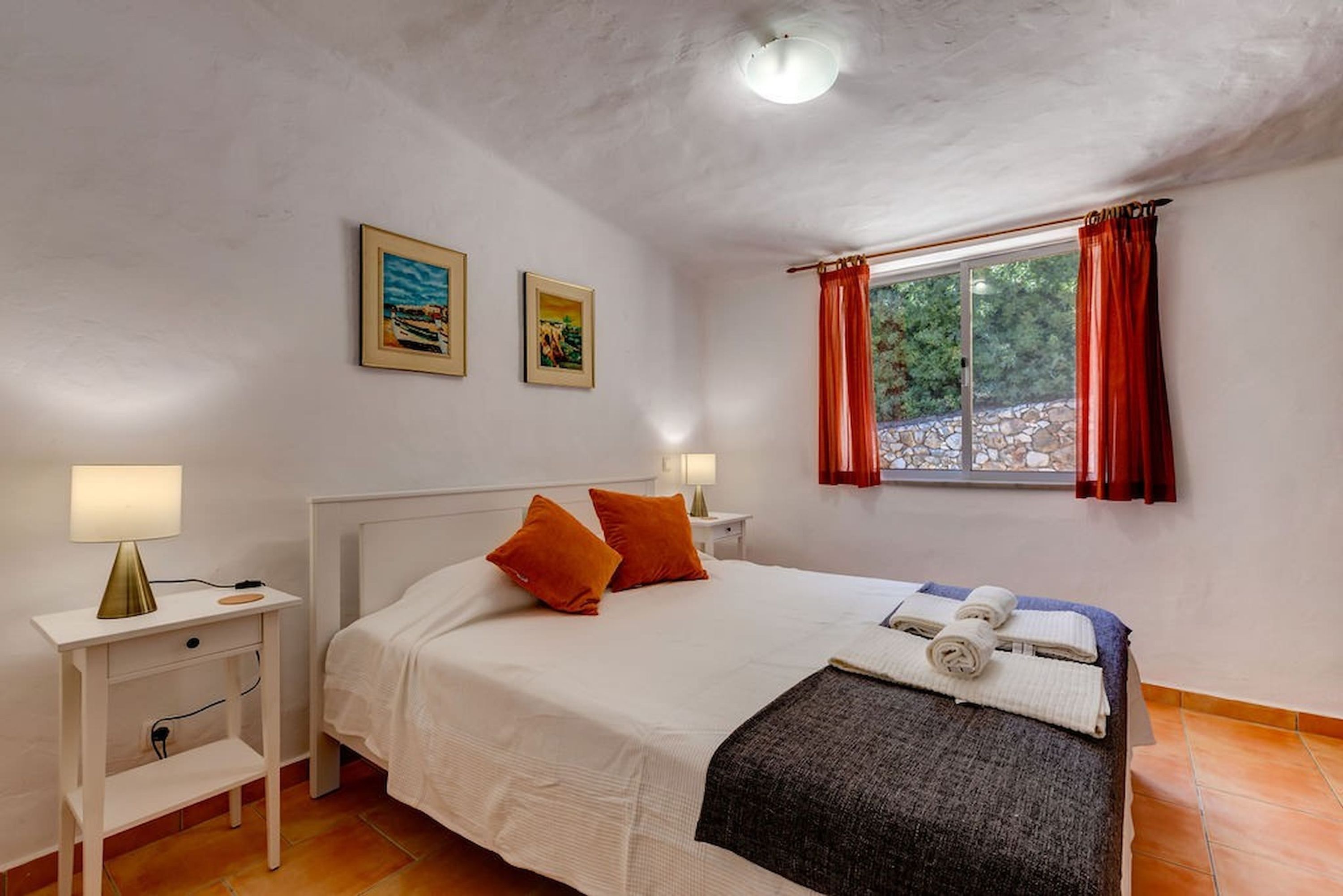 A bedroom with a bed, a nightstand, a lamp, and a window with curtains.