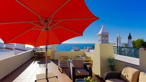 Una terraza en la azotea con un paraguas rojo, muebles de mimbre y vistas al mar.