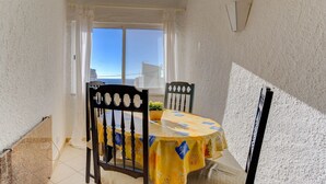 Un pequeño comedor con una mesa cubierta con mantel amarillo, dos sillas, una planta en maceta y una ventana con cortinas.