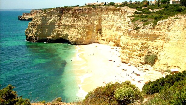 Una playa costera con acantilados, agua turquesa cristalina y una orilla arenosa.