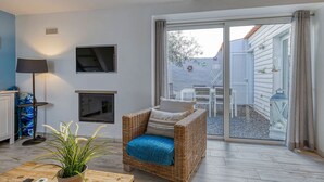 Een gezellige woonkamer met een rieten bank, een open haard, een televisie en een grote schuifdeur die leidt naar een terras.