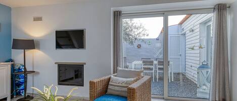 Una sala de estar acogedora con un sofá de mimbre, una chimenea, un televisor y un amplio ventanal corredizo que da a un patio exterior.