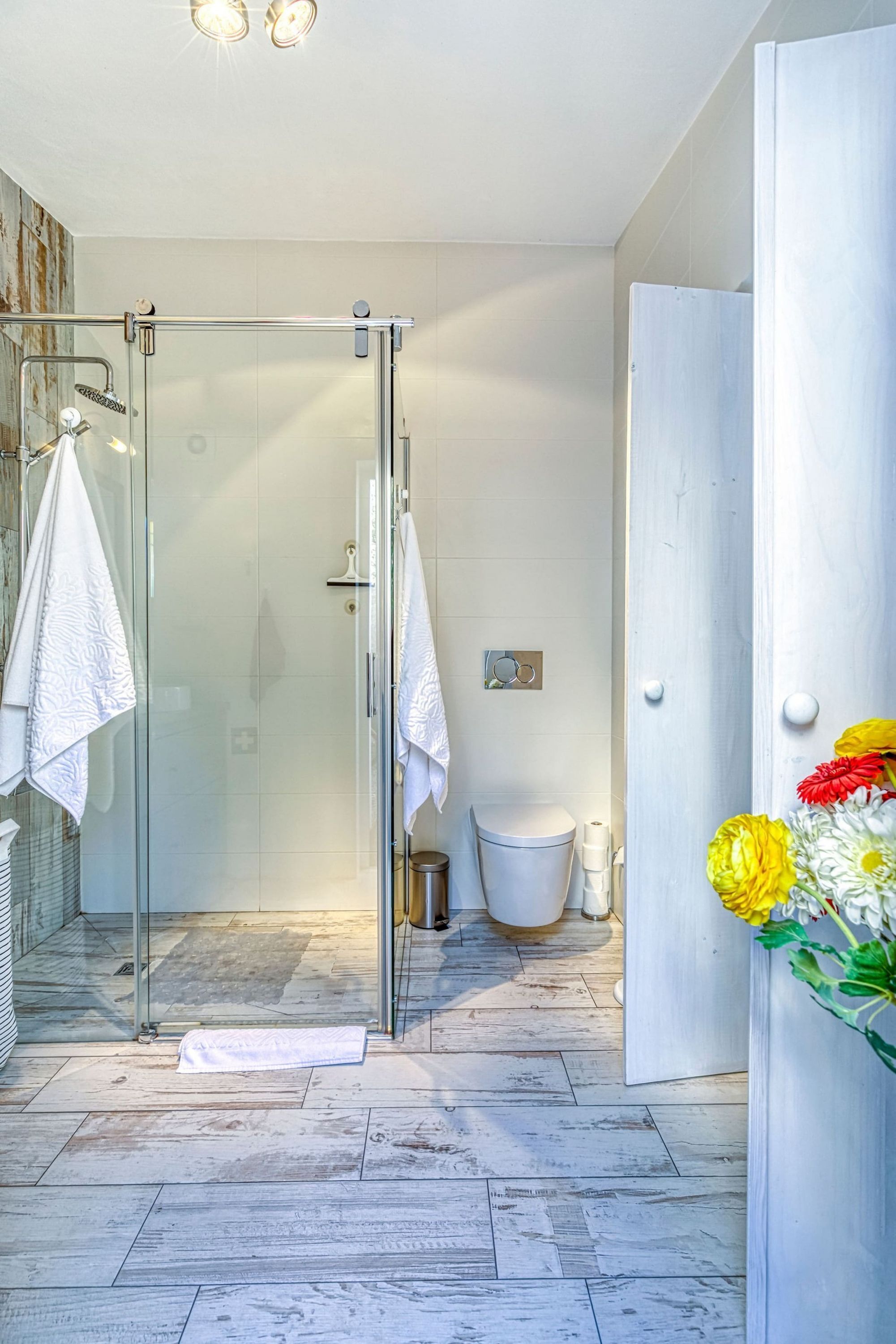 Un baño moderno con cabina de ducha de vidrio, azulejos blancos y suelo de madera.