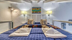 Een slaapkamer met een bed, kussens, een schilderij en wandlampen.