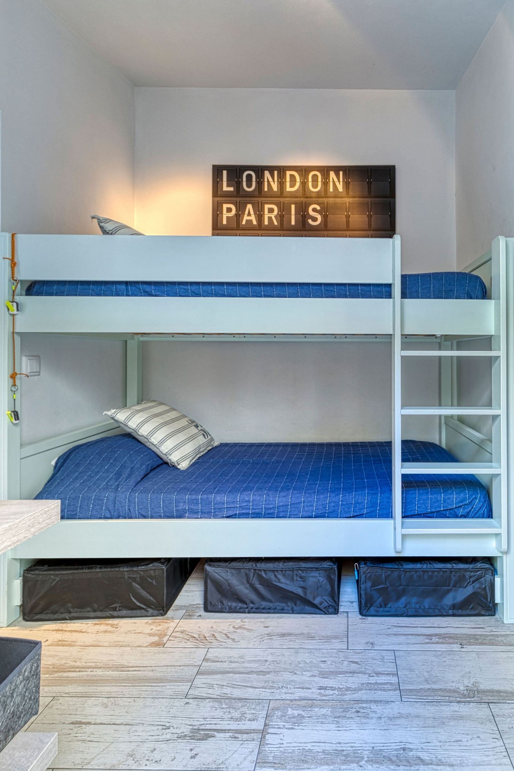 A bunk bed room with a sign that reads "LONDON PARIS" and a ladder attached to the bunk beds.