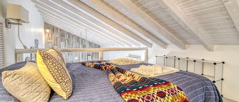 Ein Schlafzimmer mit schrägen Wänden, einem Bett mit gemusterten Betttextilien und einem Nachttisch.