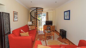A living room with a red sofa, a wooden coffee table, a television, and a spiral staircase leading to a balcony. - 6a Fabrica Velha Beautiful House Pool Walking (Lagoa)