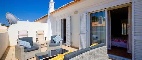 A rooftop terrace with wicker furniture, a satellite dish, and a view of a church tower.
