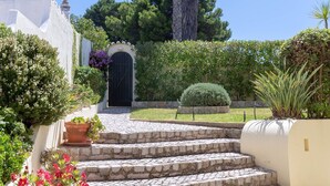 A stone staircase leading to a black door, surrounded by lush greenery and potted plants. - Silver Beautiful 4 Bedroom Vila Just Steps TO TH (Lagoa)