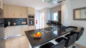 Une cuisine moderne dotée d’un îlot central, de plans de travail noirs et d’un pare-feu en verre.