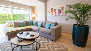 Un salon moderne avec un canapé d’angle, une table basse ronde et une grande plante en pot.