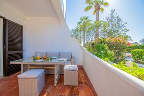 Un balcón con una mesa para dos, un banco de mimbre y vistas a follaje y palmeras.