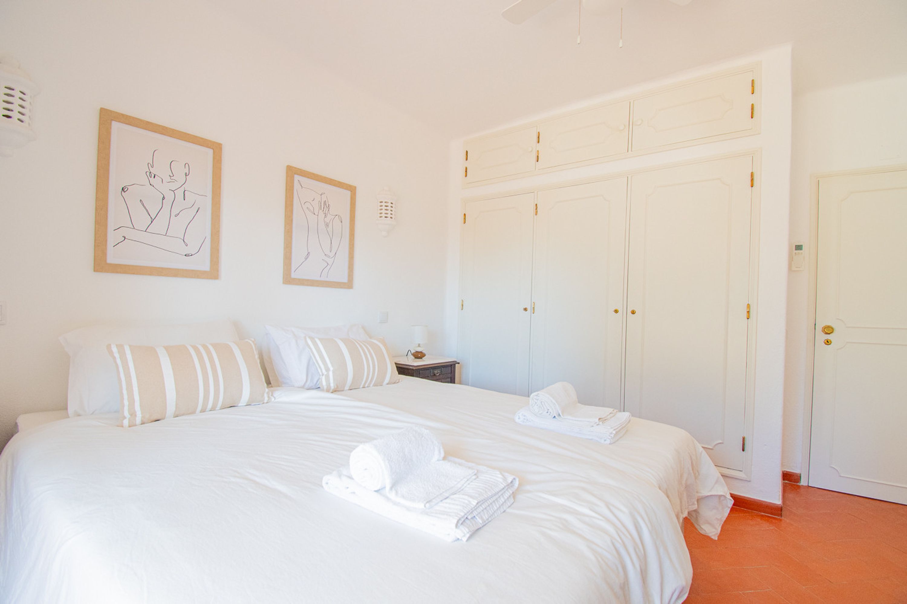 Ein Hotelzimmer mit einem großen Bett, zwei gerahmten Kunstwerken an der Wand, einem Kleiderschrank und ordentlich gefalteten Handtüchern auf dem Bett.